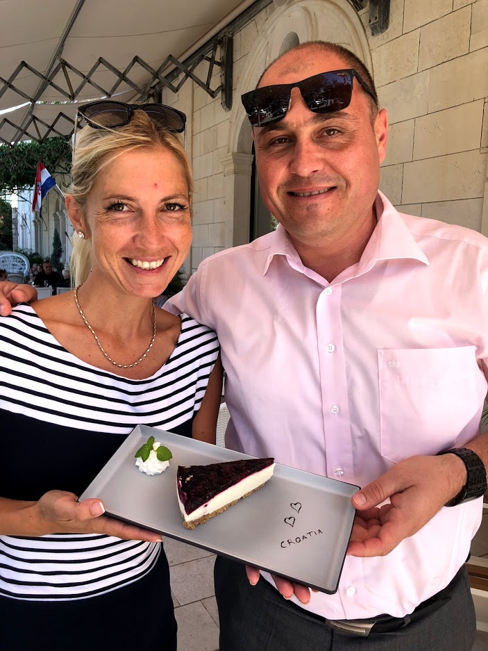 Our Concierge, Mirela, with the General Manager of the hotel. They each have a hand placed on a rectangular dish with a fresh slice of cheesecake!