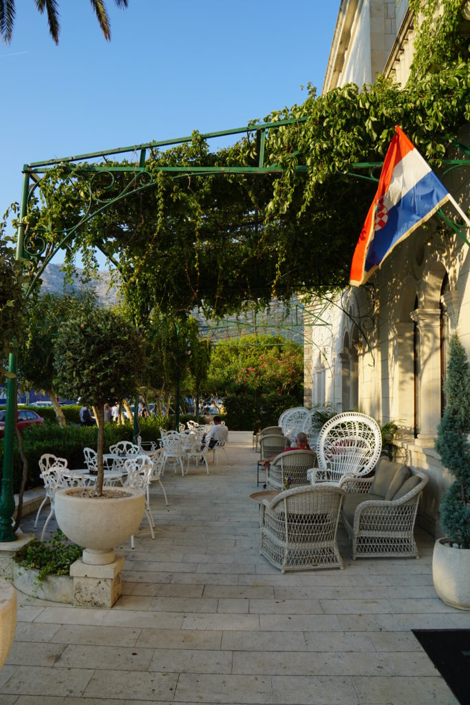 The terraced under a bright blue shade is shaded by the vines, and nearby buildings 