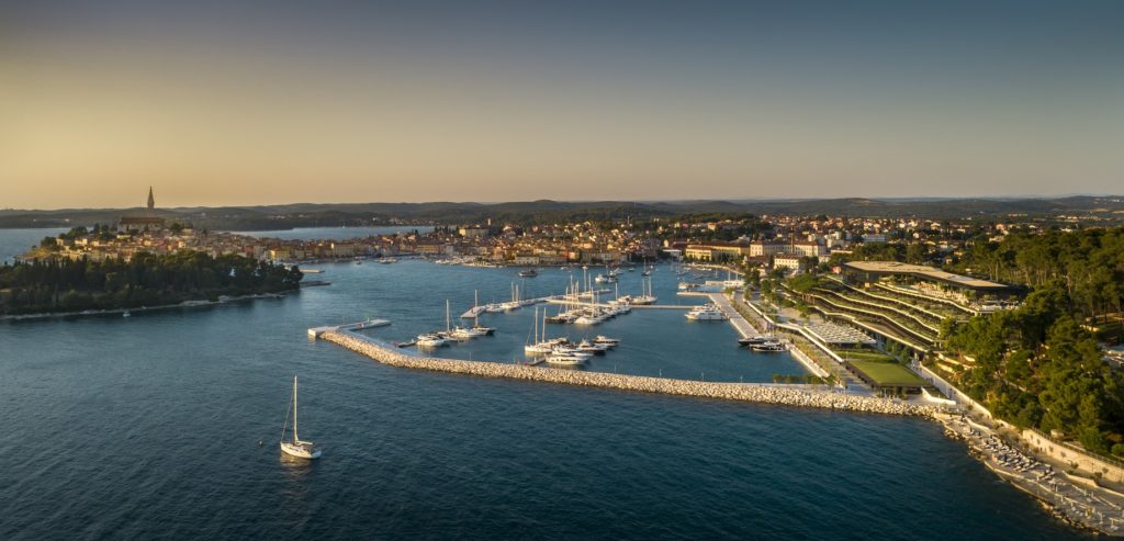 Seaside in front of Grand Park Hotel. Small marina with yachts and sailboats and the island town of Rovinj in the background.