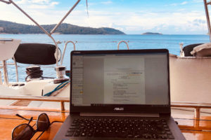 Laptop computer is open with the sea in the background. This image was taken from onboard a catamaran.
